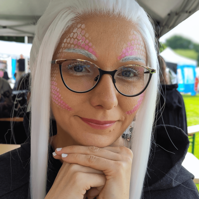Frau mit weißen, langen Haaren und Drachen-Make-up und Brille.
